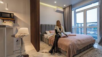 Un dormitorio moderno con una cama grande, una zona de estar con una silla y vistas a la ciudad a través de amplios ventanales.