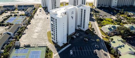 An aerial view of a hotel complex with multiple high-rise buildings, a parking lot, and tennis courts.