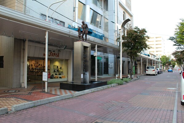 A street with a closed storefront, a statue, and parked cars. - Guest House Ichibangai Room 403 / Kitami Hokkaidō (Kitami)