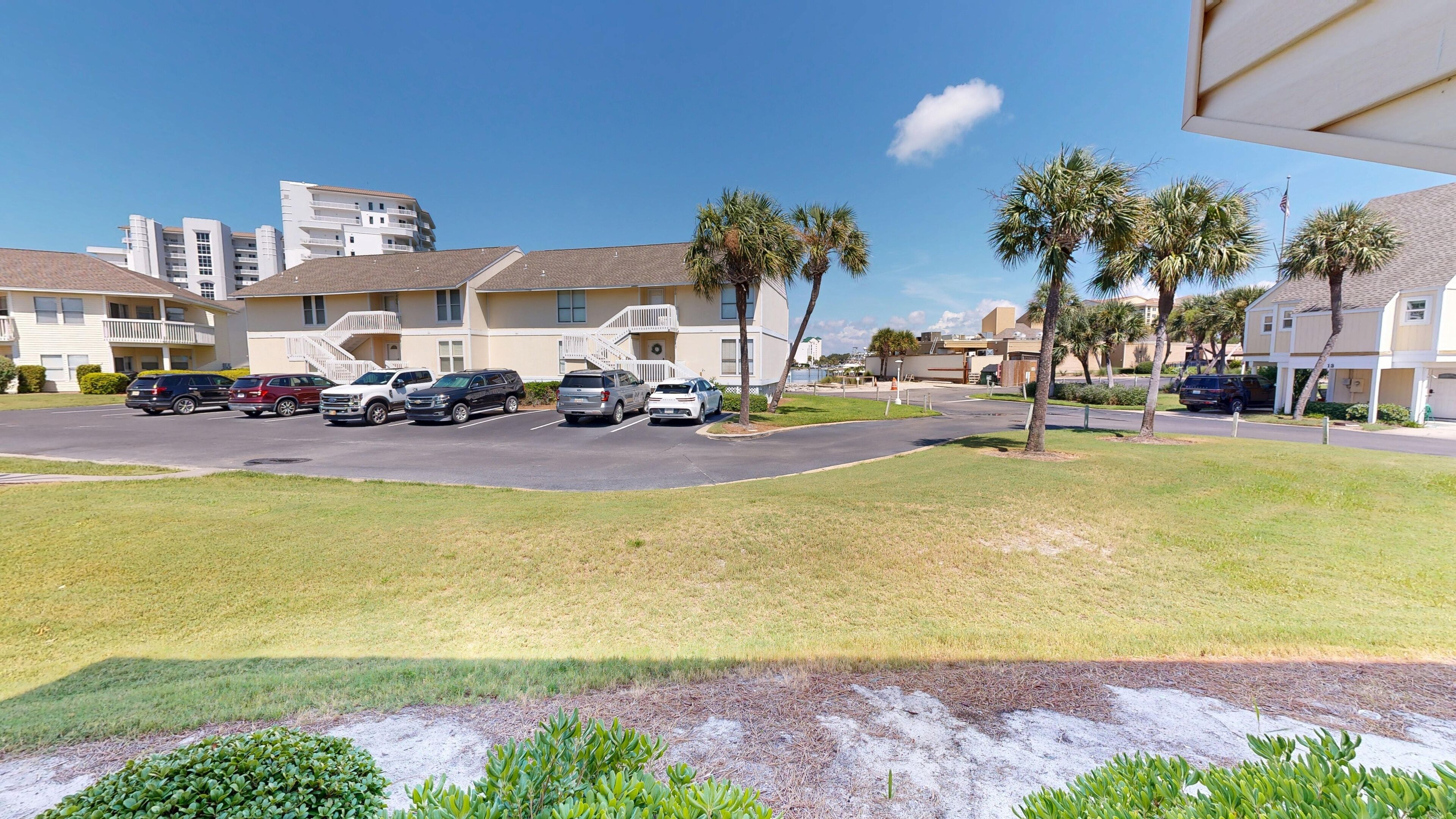 A parking lot with several SUVs and cars, surrounded by buildings with balconies and a clear blue sky.