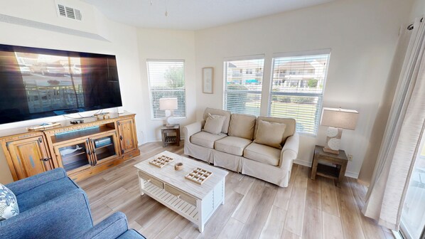 Una sala de estar con un televisor de pantalla plana grande, un sofá color beige, una mesa de centro y un sillón azul.