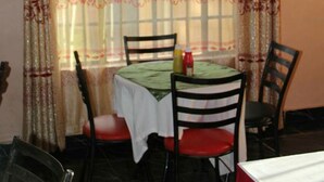 A dining area with a table set for two, chairs, and a window with patterned curtains. - The Horizon Resort (Kapenguria)