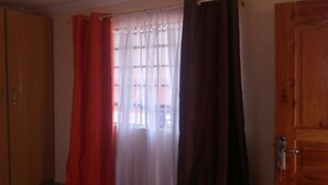 A room with a wooden door, a window with sheer white curtains, and a red curtain partially drawn. - The Horizon Resort (Kapenguria)
