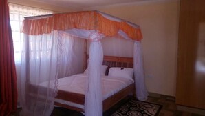 A single bed with a canopy, a bedside table, and a patterned rug. - The Horizon Resort (Kapenguria)