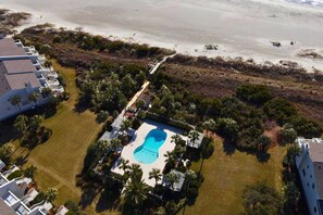 Luftaufnahme eines Resorts mit einem Swimmingpool, umgeben von Palmen und einem Strand.