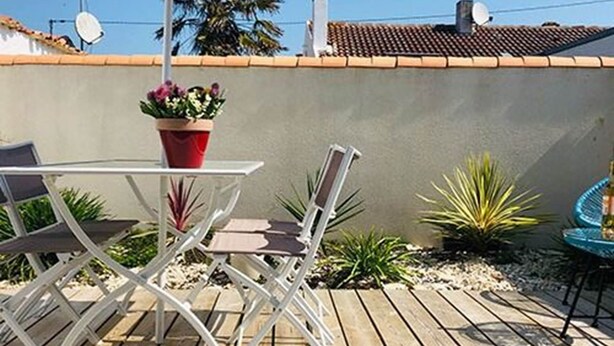 A wooden deck with a table and chairs, surrounded by potted plants and a small table with a bottle. - LA MAISONNETTE, Gîte 5. Clos des Aigrettes, 30m from La Cotinière Port (ST PIERRE D'OLERON)