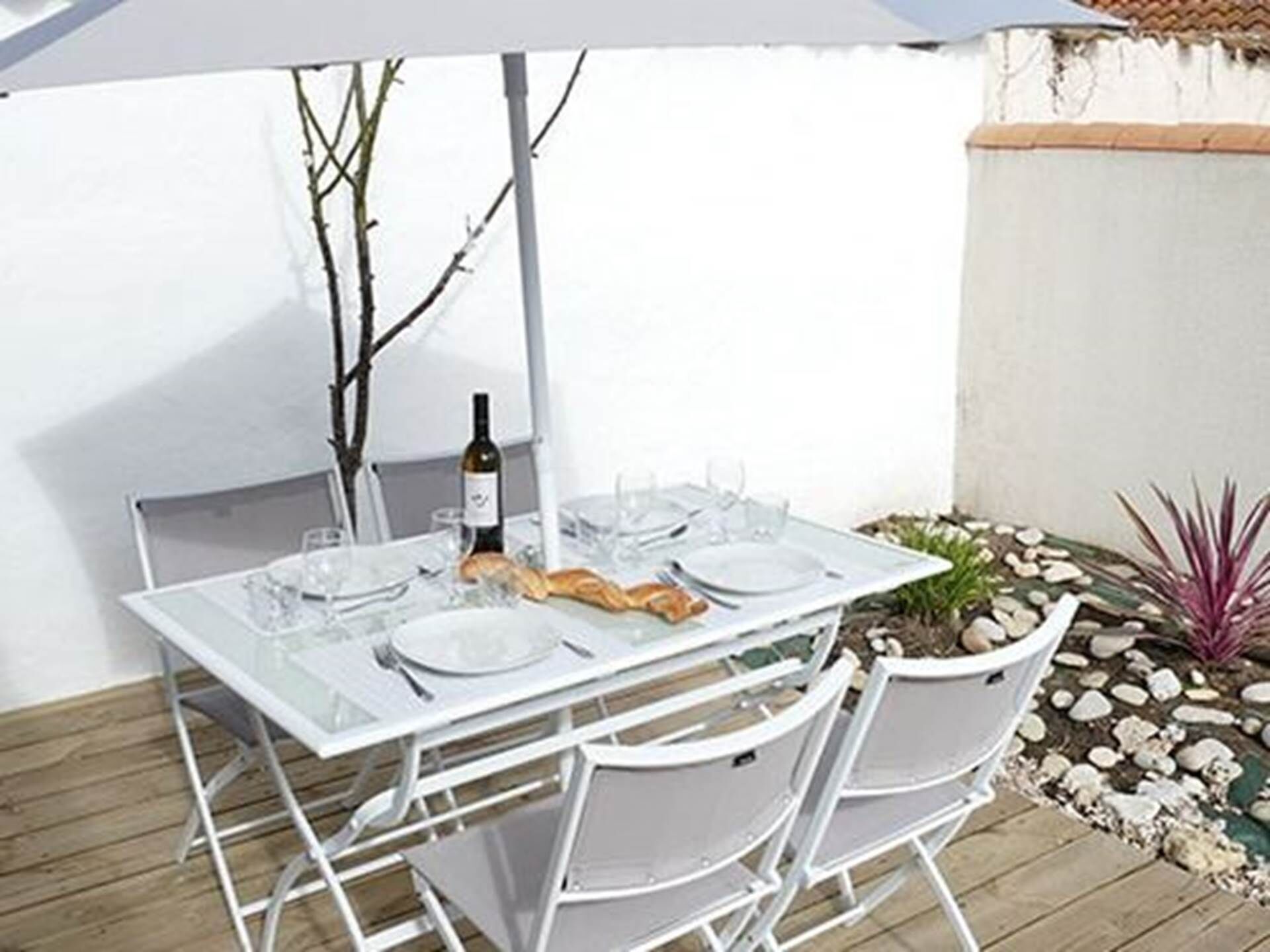 Une table blanche dressée à l’extérieur, avec une bouteille de vin, des verres et une baguette.