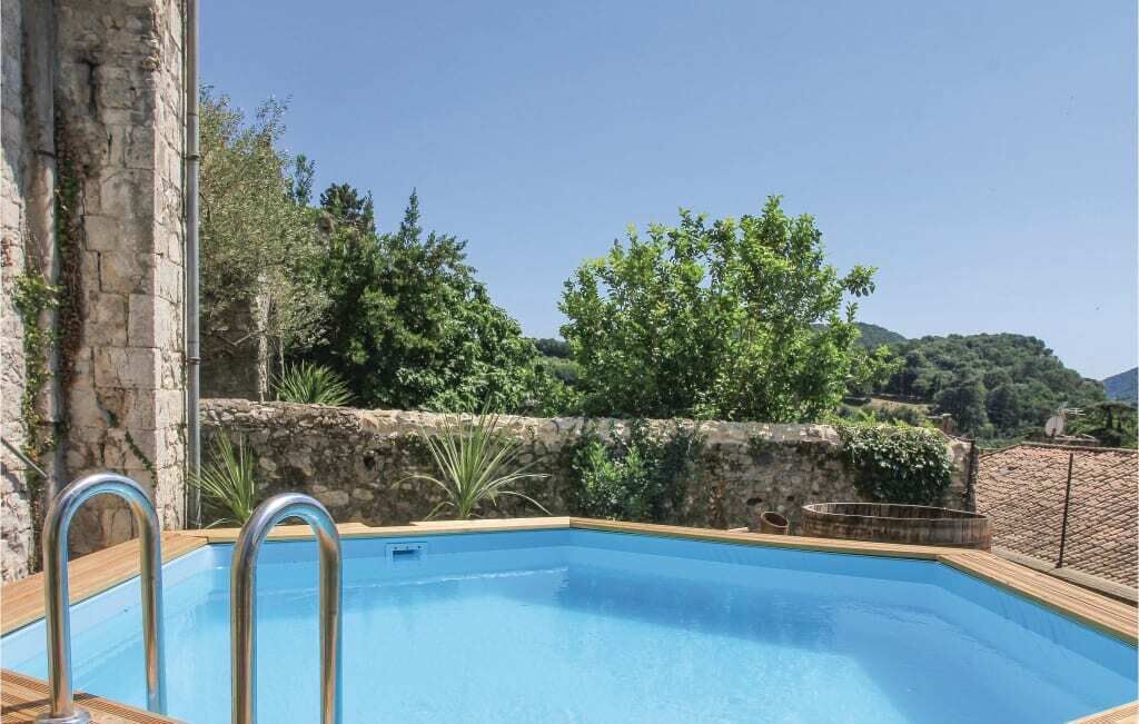Ein rechteckiger Pool mit Metallleitern, umgeben von Steinmauern und Pflanzen, mit Blick auf Bäume und Hügel im Hintergrund.