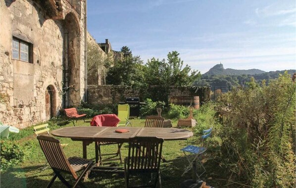 Un área de comedor al aire libre con encanto, con una mesa redonda y sillas, rodeada de vegetación y un edificio de piedra.