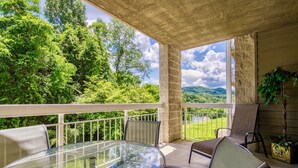 A covered outdoor area with a glass table and chairs, surrounded by a white railing, overlooking a lush green landscape. - FREE Dollywood Ticket • Whispering Pines 322 •  2bd/2ba • Mountain View • Pools (Pigeon Forge)
