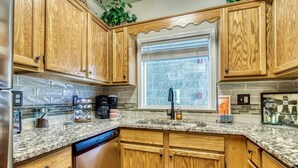 A kitchen with wooden cabinets, granite countertops, a dishwasher, and a window with blinds. - FREE Dollywood Ticket • Whispering Pines 322 •  2bd/2ba • Mountain View • Pools (Pigeon Forge)