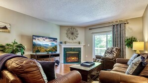A living room with leather sofas, a fireplace, a television, and a large window with curtains. - FREE Dollywood Ticket • Whispering Pines 322 •  2bd/2ba • Mountain View • Pools (Pigeon Forge)