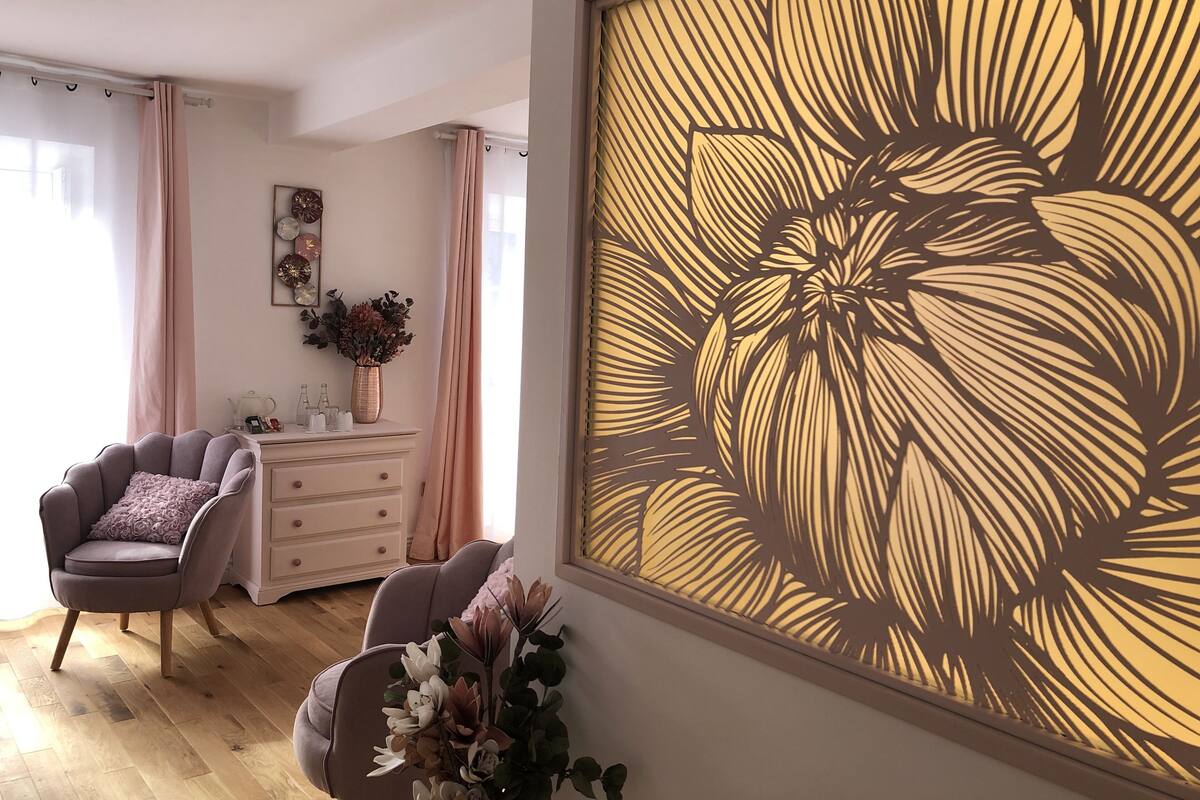 Quarto com uma grande obra de arte floral na parede, uma cadeira, um penteado e um vaso com flores.