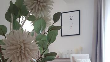 A room with a large vase of flowers, a white sofa, a white armchair, and a dresser in the background.