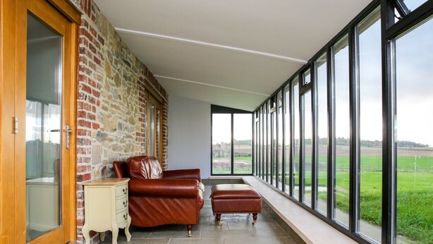 Ein Zimmer mit Steinwand, Ledersofa, Holzschrank und großem Fenster mit Blick auf ein grünes Feld.