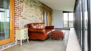 Ein Zimmer mit Steinwand, Ledersofa, Holzschrank und großen Fenstern.