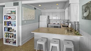 A compact kitchen with a central island, white cabinetry, and a built-in bookshelf. - "Commodores 101" | Corner Unit w/ Beach Views | Community Pool | Beach Chairs included (Santa Rosa Beach)