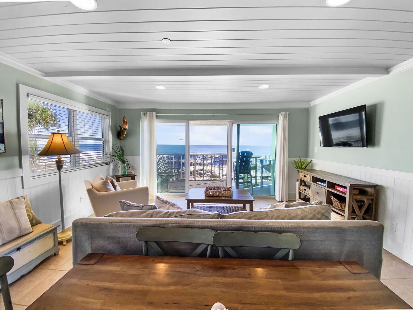 A spacious living room with a large sofa, a coffee table, and a TV mounted on the wall.