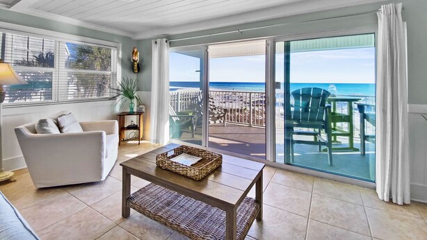 A spacious living room with a white sofa, a wooden coffee table, and a large sliding glass door leading to a balcony with a view of the ocean. - "Commodores 101" | Corner Unit w/ Beach Views | Community Pool | Beach Chairs included (Santa Rosa Beach)
