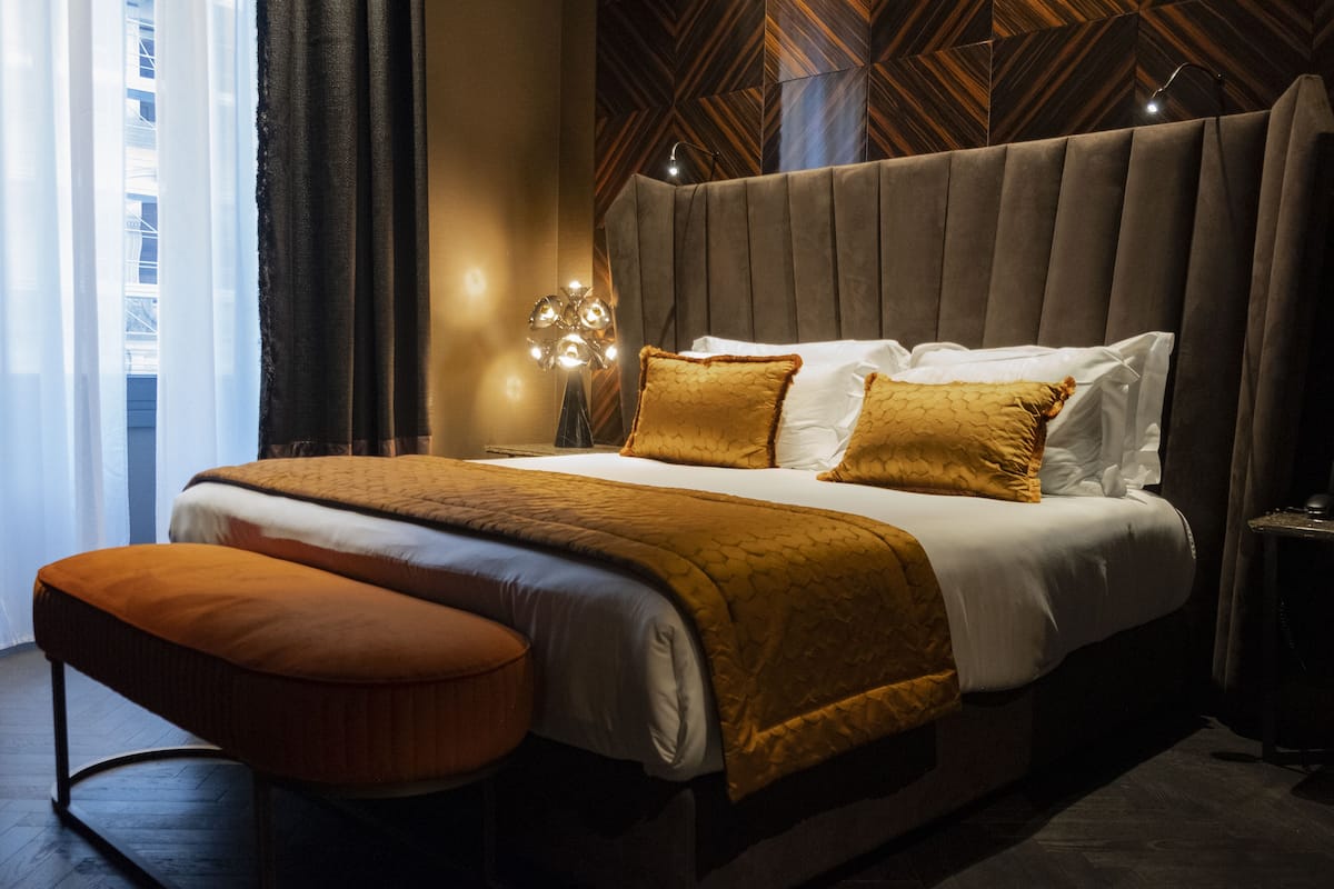 A modern hotel room with a large bed, a bedside table, and a view of the city through the window.