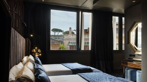 A hotel room with two beds, a large window with a view of buildings, a desk with a lamp, and a small window on the right. - U-Visionary Roma Hotel (Rome)