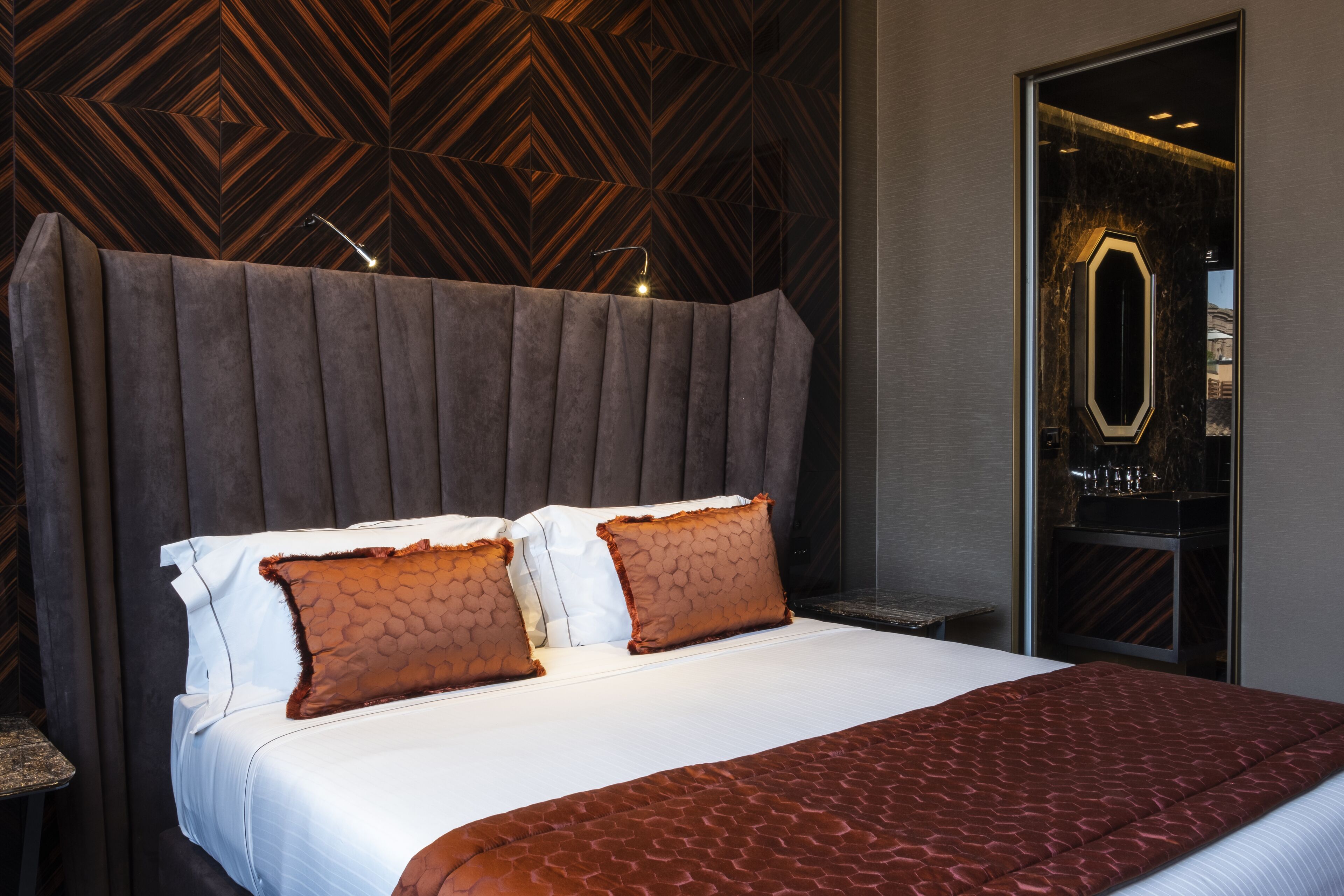 A modern hotel room with a large bed, a wooden-patterned headboard, and a mirror above the bed.