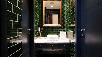 Een badkamer met een wit wastafelmeubel, donkere kastjes en groene betegelde wanden.