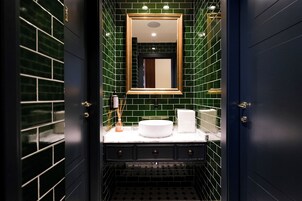 Un bagno con un lavandino bianco, mobili scuri e pareti rivestite di piastrelle verdi.