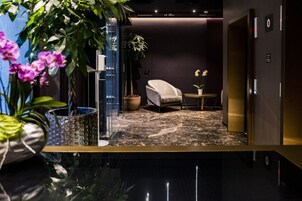 Una moderna hall d'hotel con pavimento in marmo, un'area salotto con un divano e un tavolino, e un'ampia pianta in vaso.