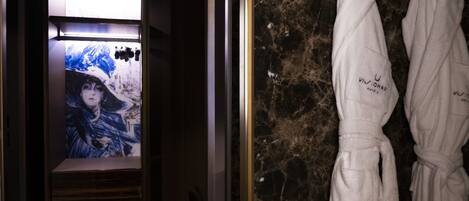 A bathroom with a marble wall, a shower area, and two white robes hanging on hooks.