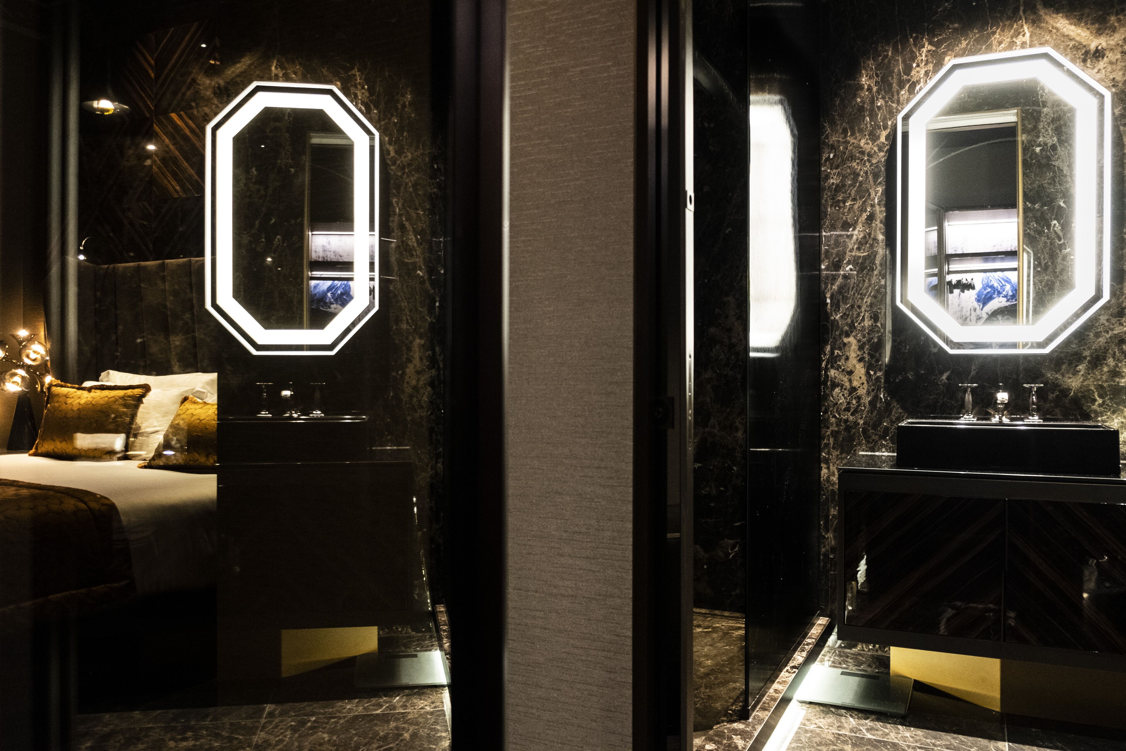 A modern hotel room with a large bed, a nightstand, a mirror with illuminated frame, and a marble floor.
