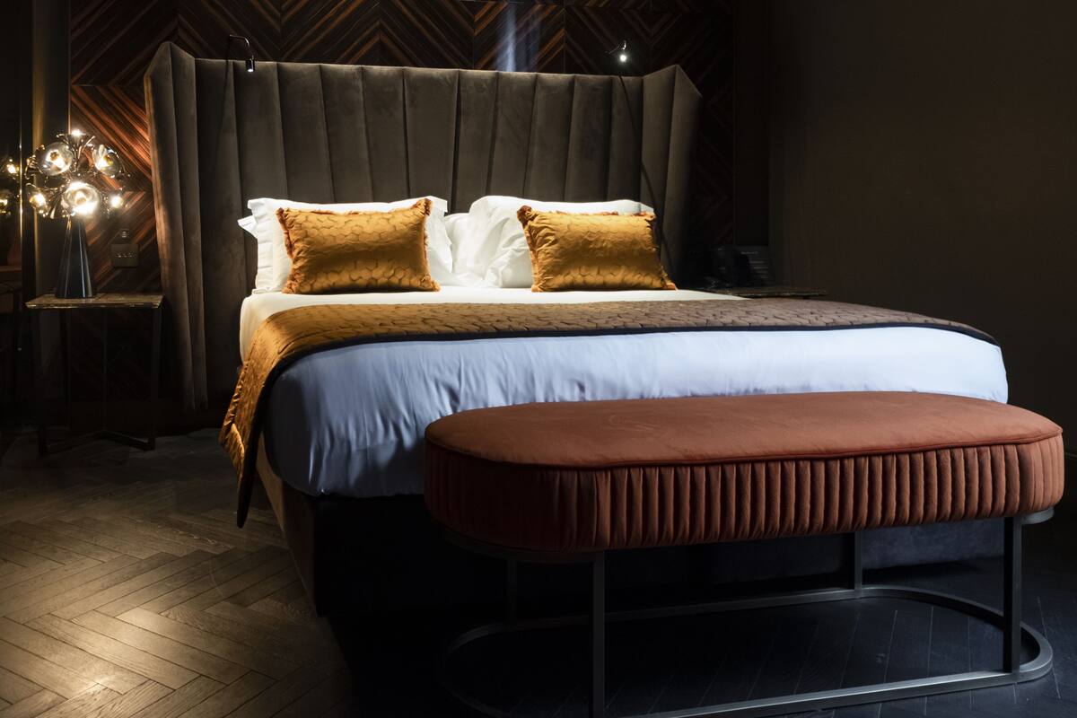 A modern bedroom with a large bed, two pillows, a bench, and a nightstand with a lamp.