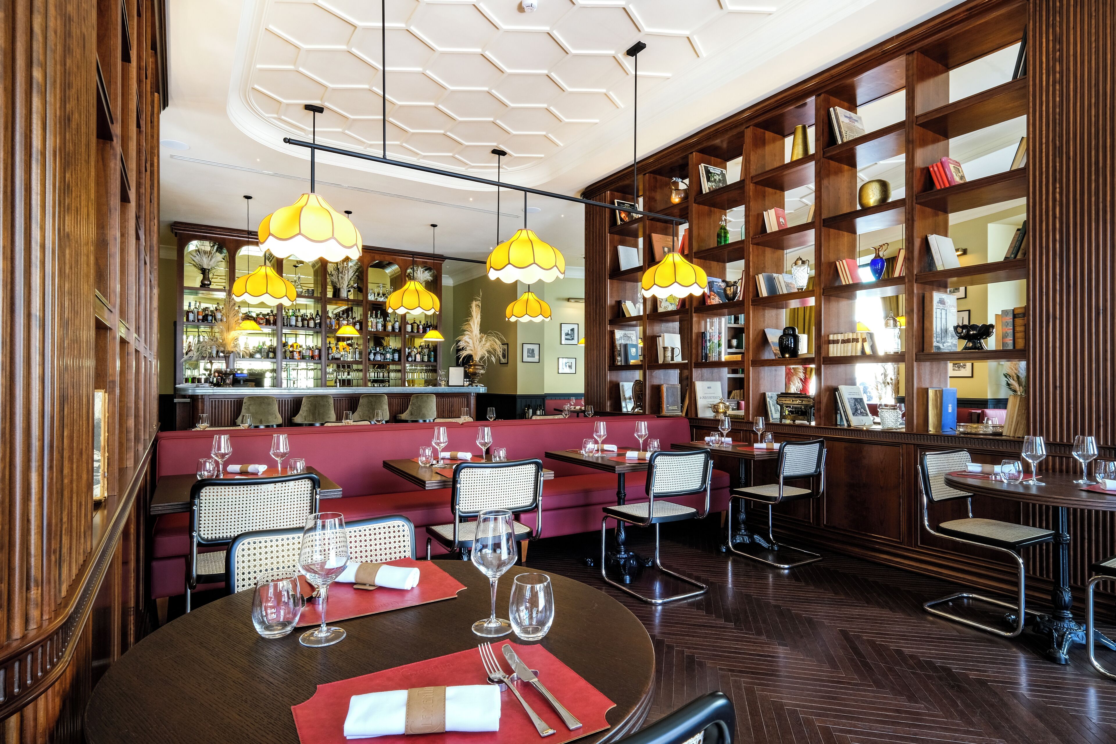 Un restaurant amb prestatgeries de fusta, seients vermells i llums penjants grogues.