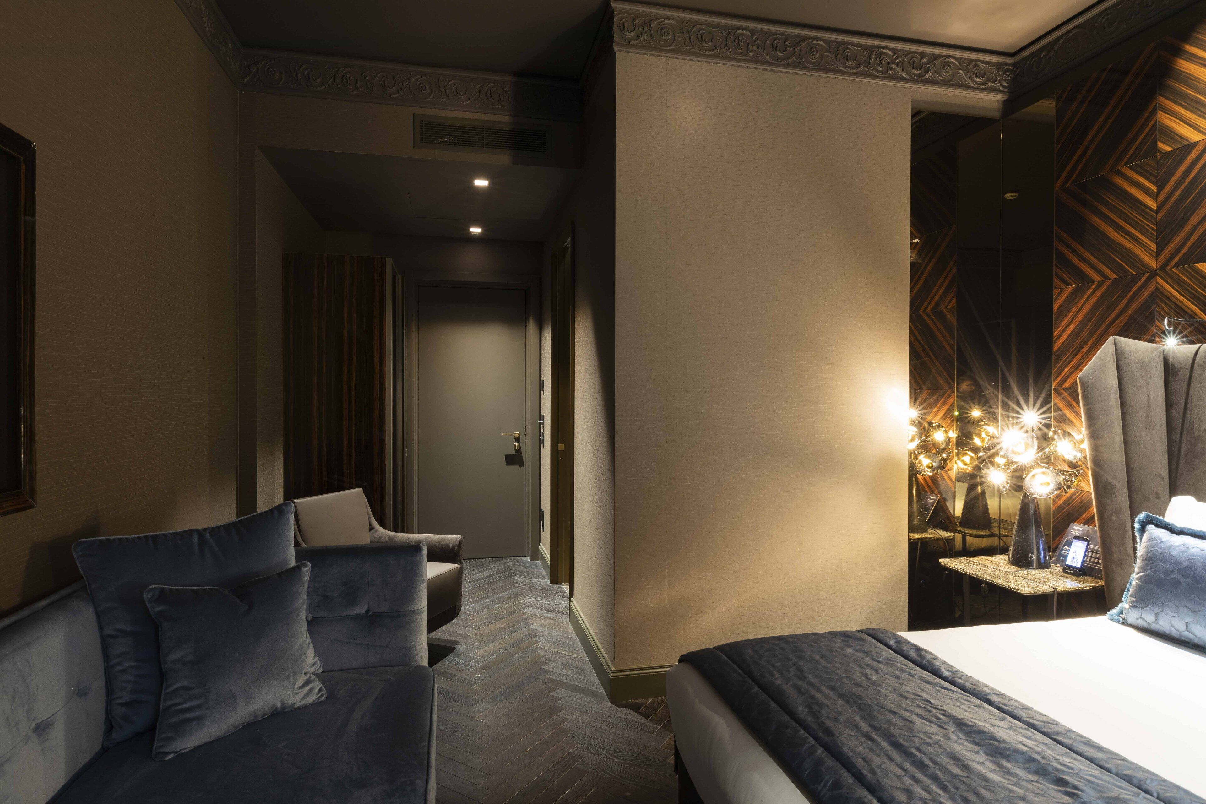A hotel room with a bed, a sofa, and a small table with a lamp.