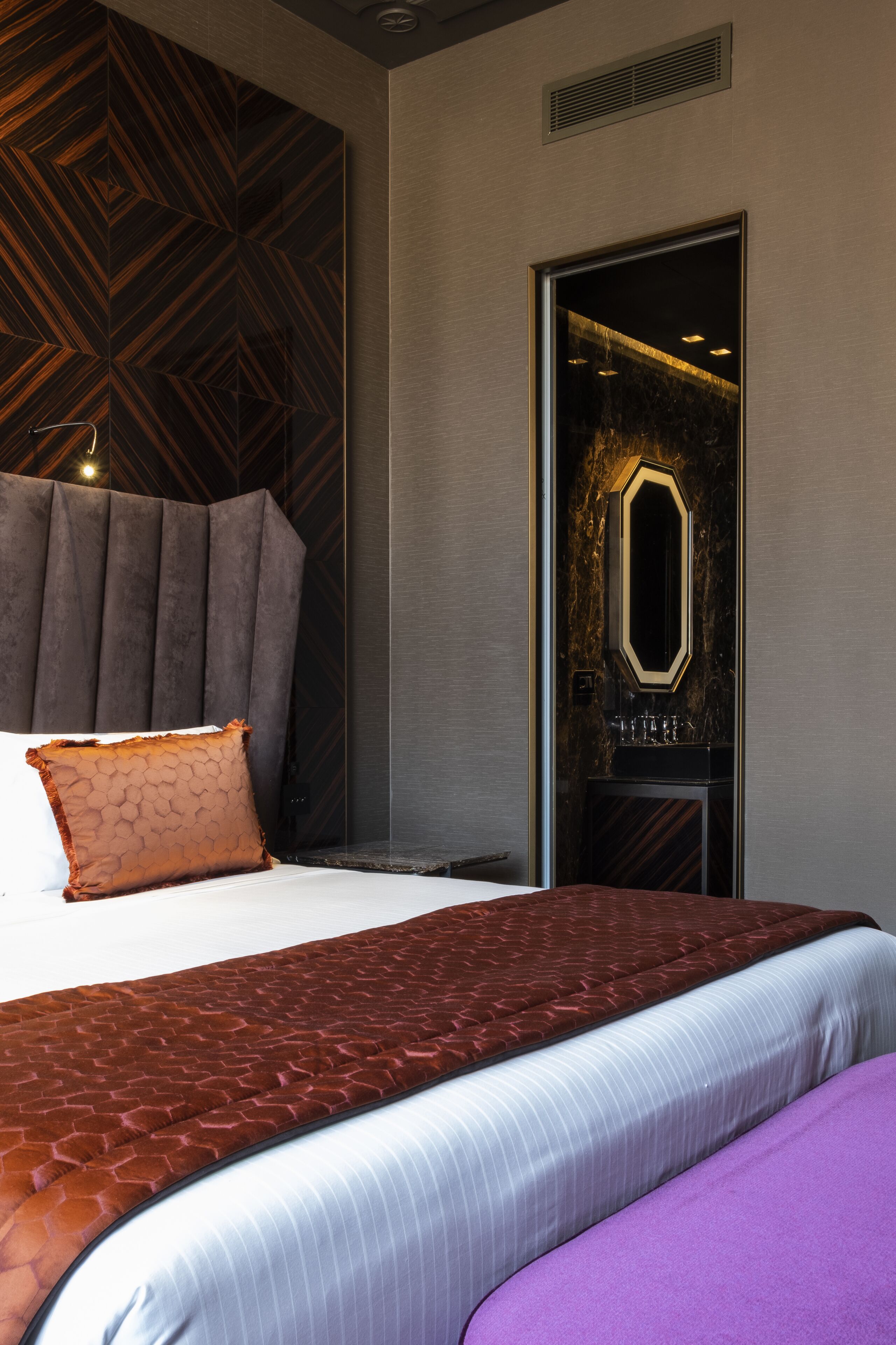 Ein Hotelzimmer mit einem großen Bett, einem Kopfteil, einem Spiegel und einer Tür mit geometrischem Muster.