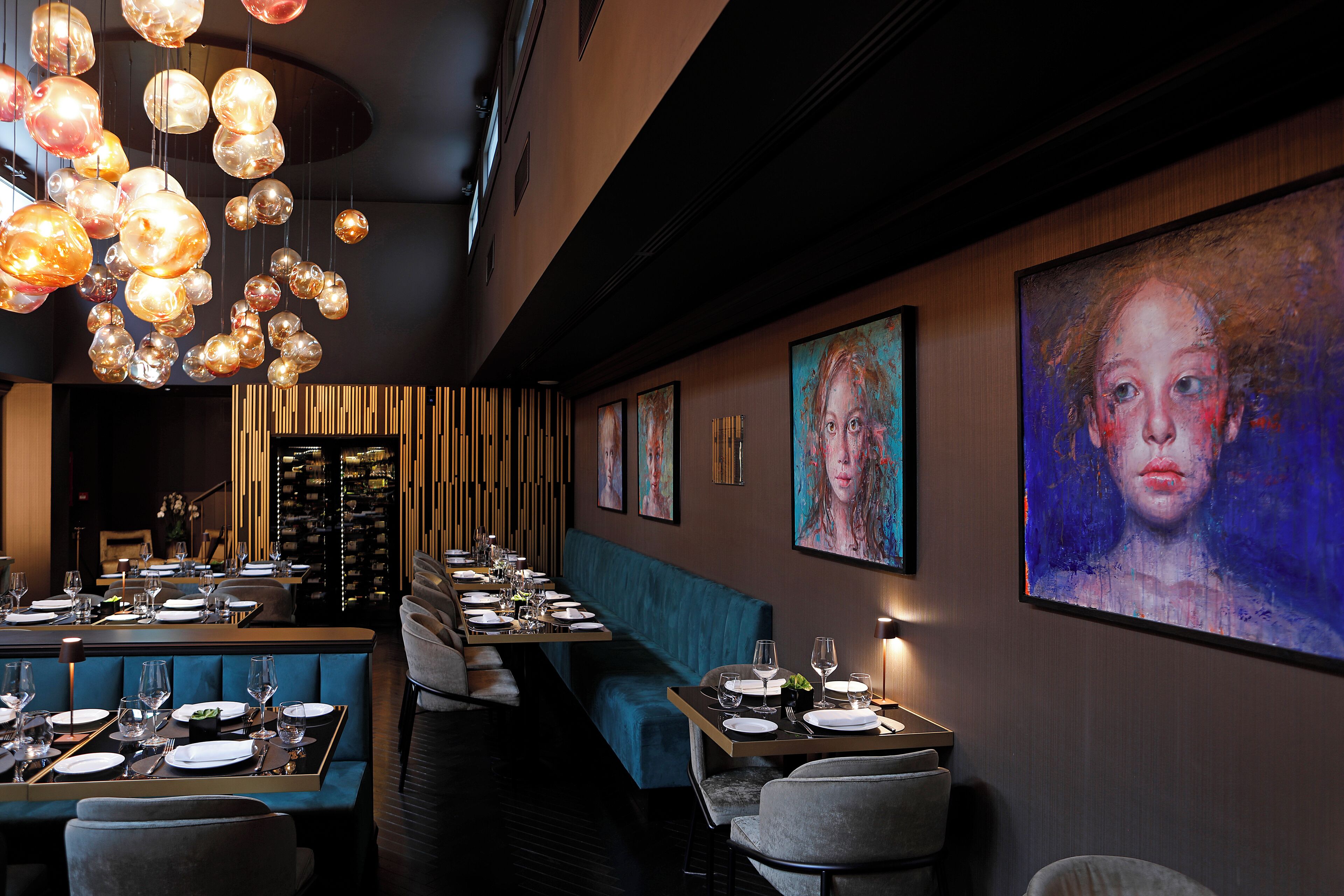 En restaurant med et langt spisebord, et siddeområde med blå båse og en væg med indrammede kunstværker.