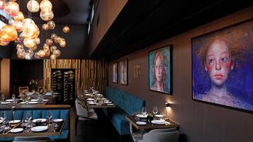 Un restaurante con una larga mesa dispuesta para comer, una zona de asientos con asientos tipo cabina en azul y una pared decorada con cuadros.