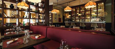 Un restaurant avec des banquettes rouges, des étagères en bois et des lampes orange suspendues au plafond.