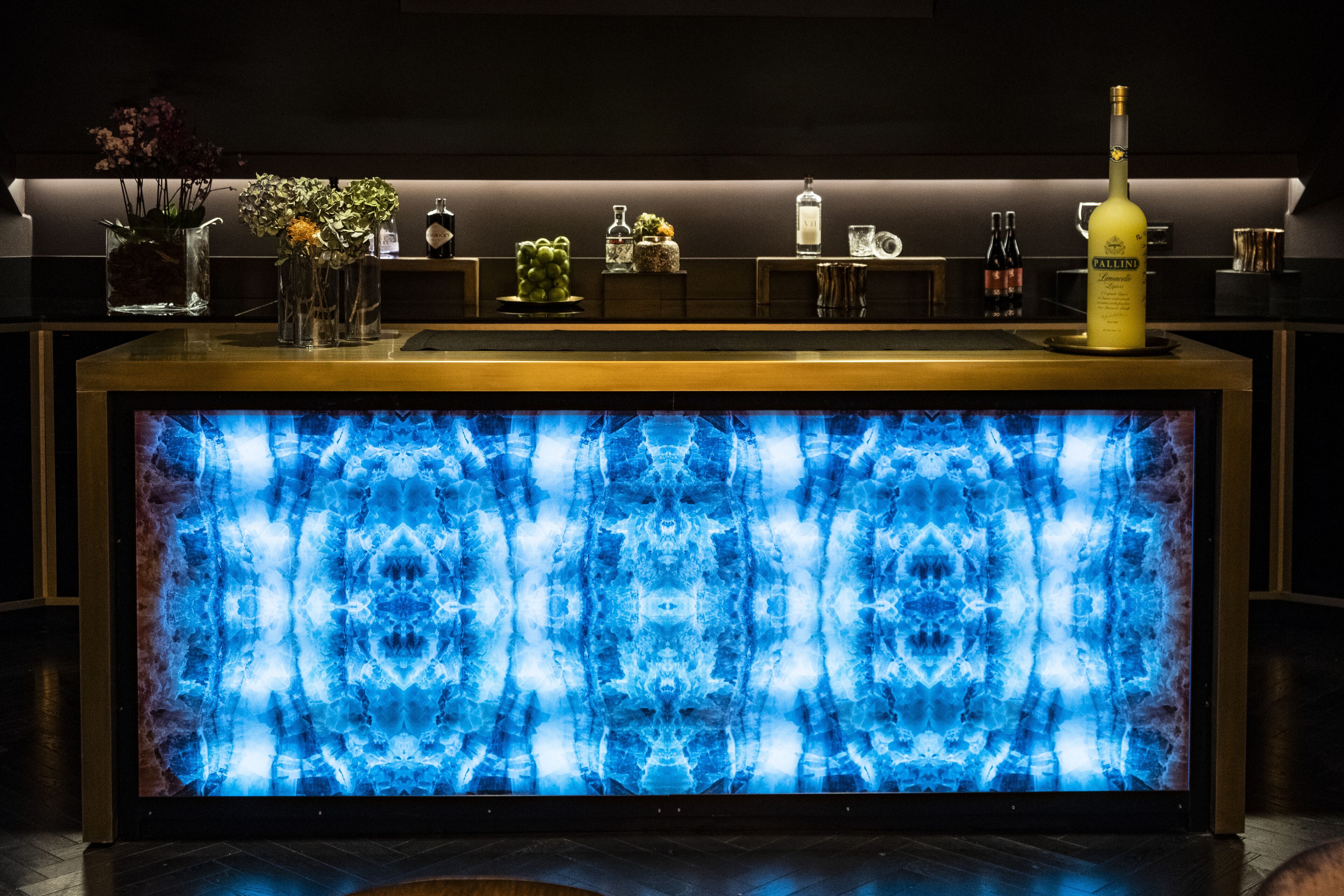 Eine Barbereich mit einer blauen beleuchteten Platte, verschiedenen Flaschen und einer Blumenvase.