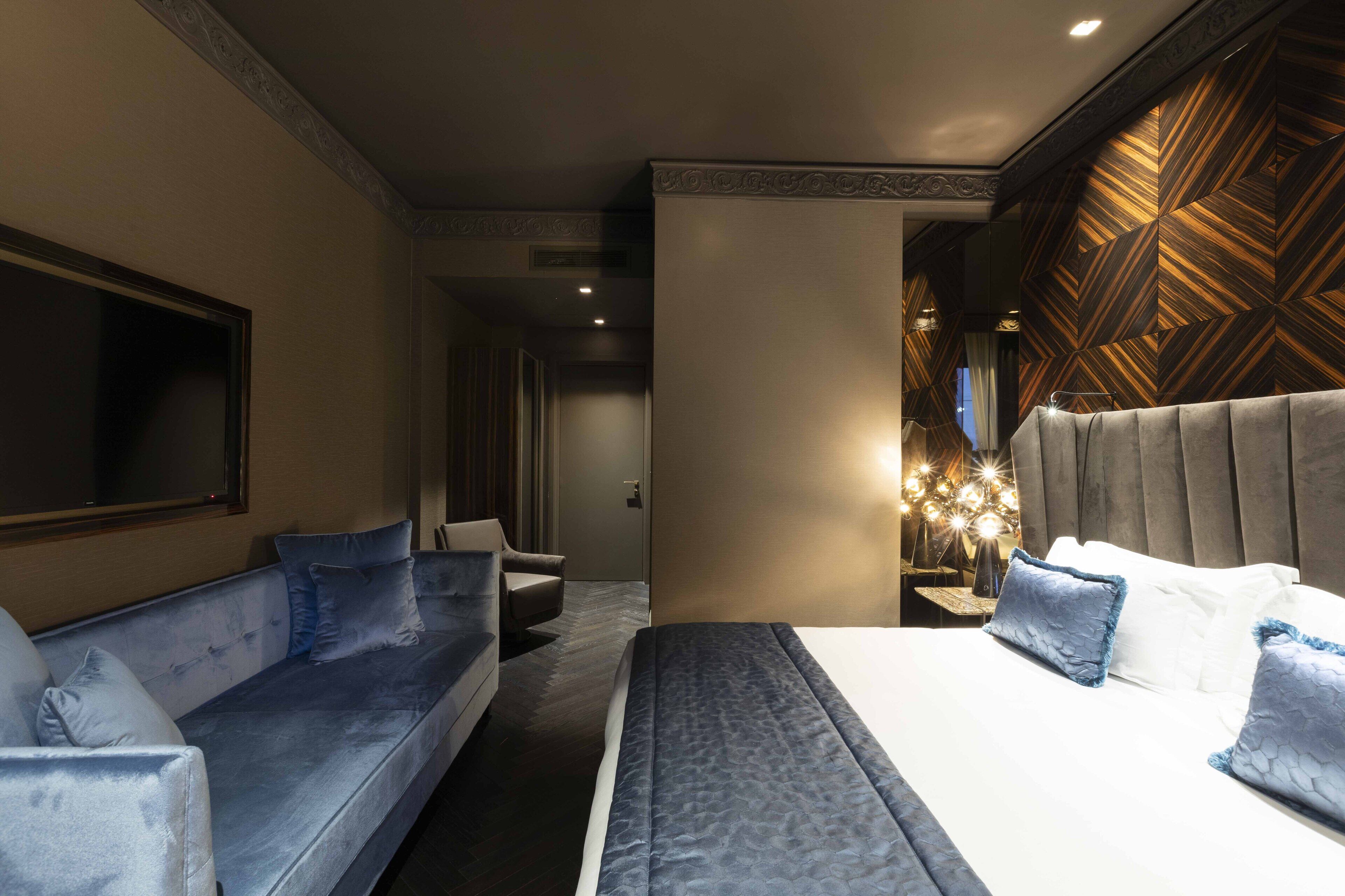 A modern hotel room with a large bed, a sofa, and a TV.