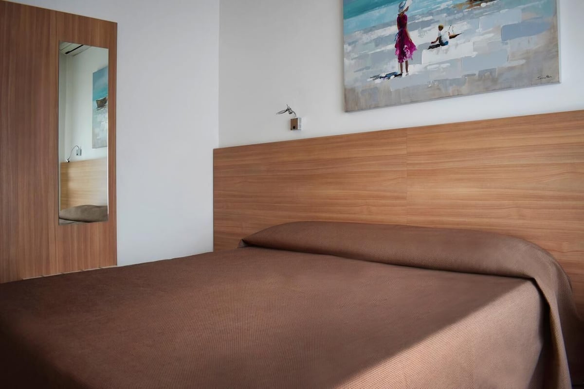 A bedroom with a wooden headboard, a bed with brown bedding, a painting on the wall, and a mirror on the door.
