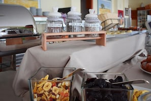 Una mesa de buffet con frascos etiquetados de frutos secos y un bol de vidrio con mezcla de nueces.