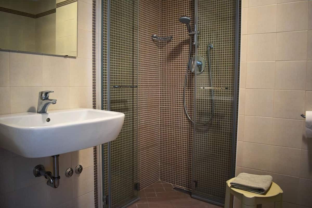 A bathroom with a white sink, a shower enclosure with a glass door, and a small stool with a towel.