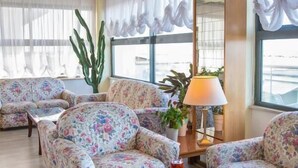 A living room with floral-patterned sofas, a glass coffee table, a lamp, and a cactus plant. - Hotel Igea Spiaggia (Bellaria-Igea Marina)
