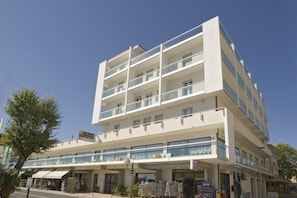 Un hotel de varios pisos con diseño moderno, que cuenta con balcones en cada planta y un espacio comercial en la planta baja.