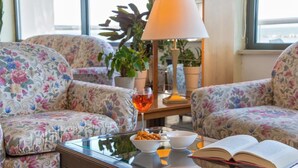 A room with floral-patterned sofas, a glass coffee table, a bowl of snacks, a glass of red drink, and an open book. - Hotel Igea Spiaggia (Bellaria-Igea Marina)