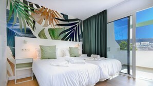 A modern hotel room with a large bed, a nightstand, and a view of the city through the glass door. - Palm Suites (Mogan)