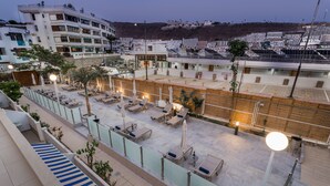 A rooftop terrace with sun loungers, a pool, and a view of the cityscape. - Palm Suites (Mogan)