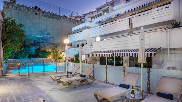 A rooftop pool area with lounge chairs and umbrellas, a pool, and a view of a rocky landscape. - Palm Suites (Mogan)