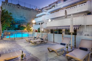 A rooftop pool area with lounge chairs and umbrellas, a pool, and a view of a rocky landscape. - Palm Suites (Mogan)
